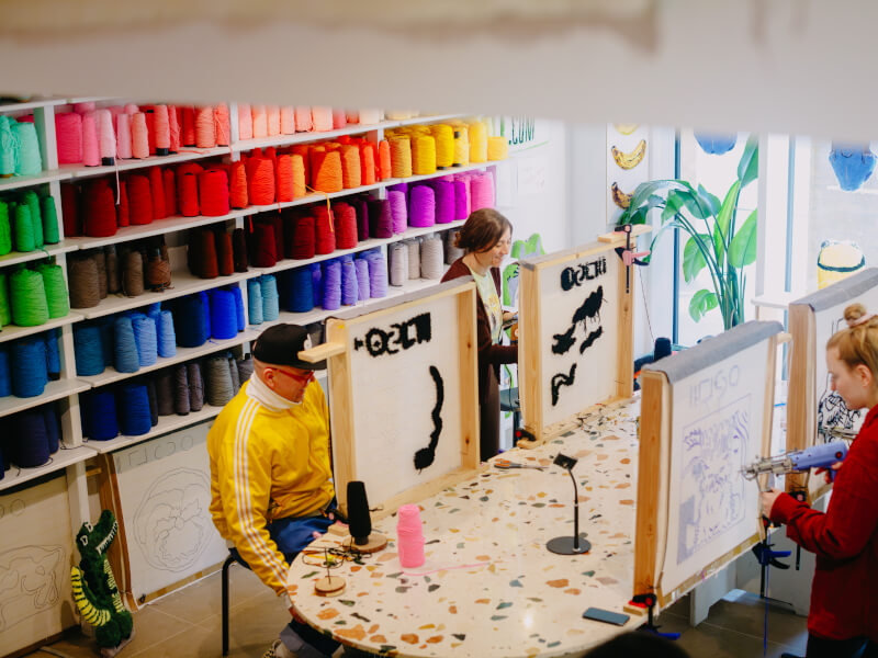 A shot from above of a tufting studio, featuring four students at canvases, making handmade rugs